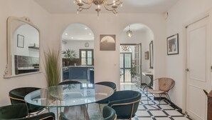 Uma sala de jantar com mesa de vidro, cadeiras escuras, um candelabro e chão xadrez.