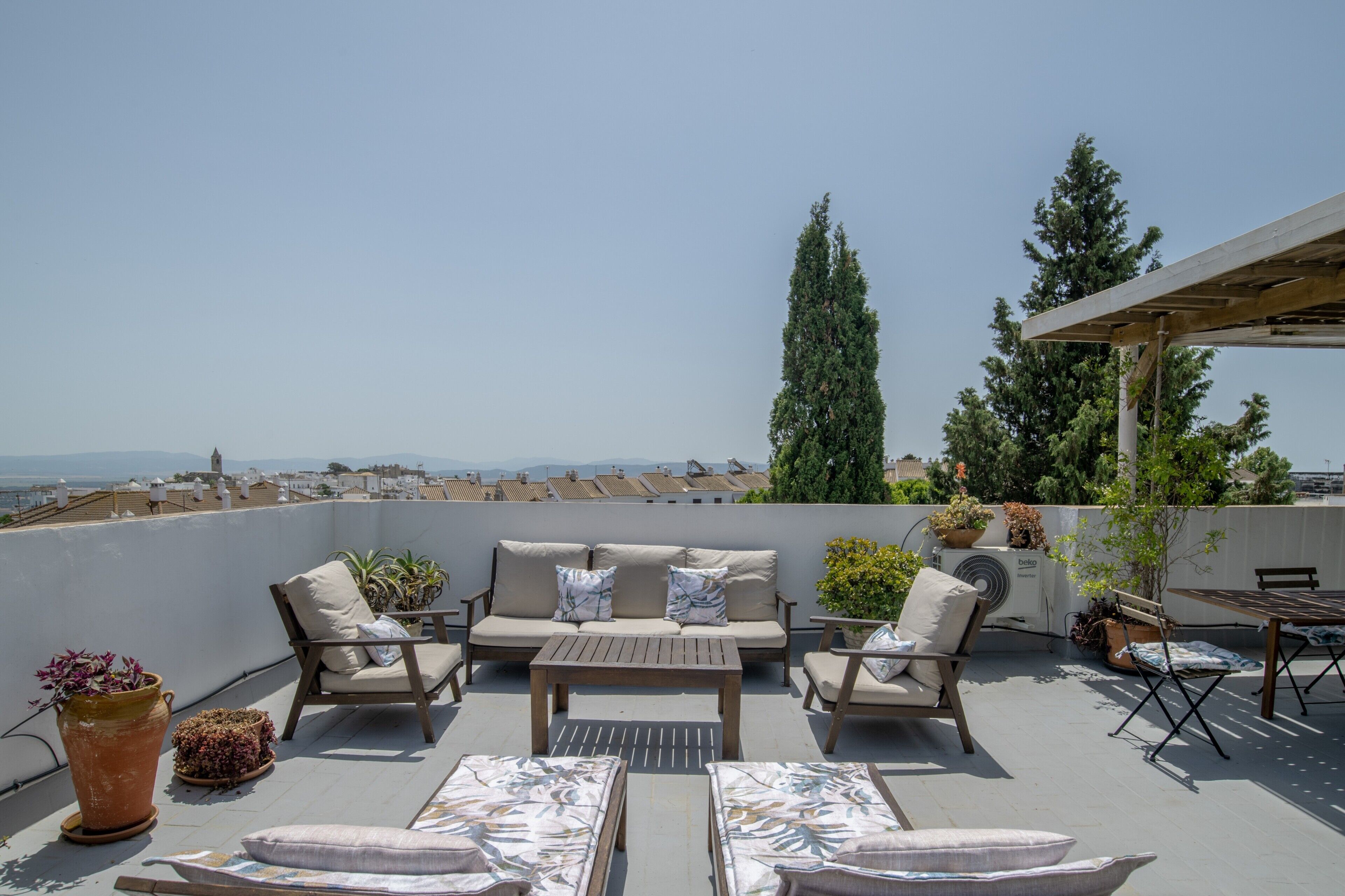 A rooftop terrace with a sofa set, a table, and potted plants.