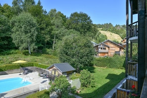 A residential area with a swimming pool, wooden houses, and a hill in the background. - Apartment 'L’ourson' with Mountain View, Shared Pool and Wi-Fi (Les Déserts)