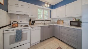 A kitchen with white cabinets, a stove, a microwave, and a window. - The Green Acres Cottage - Charming 2 Bedroom near S&T and Acorn Trail in Rolla. (Rolla)
