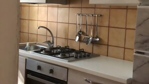 Een keuken met een gasfornuis, oven, spoelbak en hangend keukengerei.