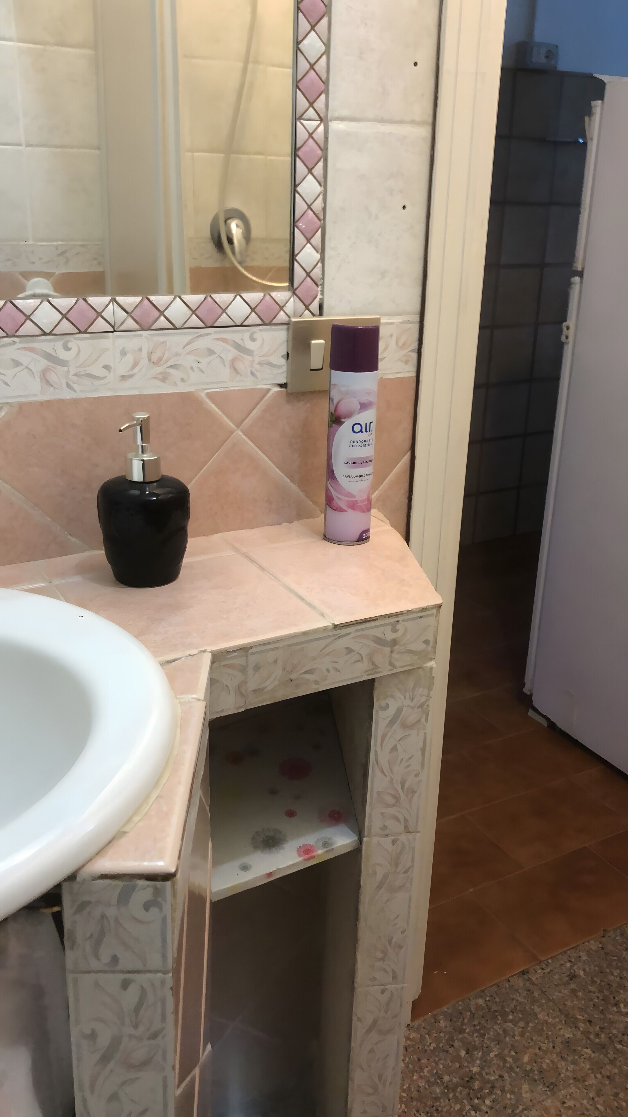 Un baño con un lavamanos blanco, un dispensador de jabón negro y una lata de desodorante en el tocador.