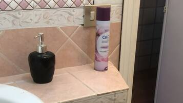 Un baño con un lavamanos blanco, un dispensador de jabón negro y una lata de desodorante en el tocador.