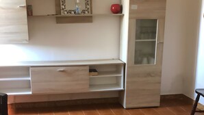 Een kamer met een houten kast, een zwart poef en een plank met decoratieve objecten.