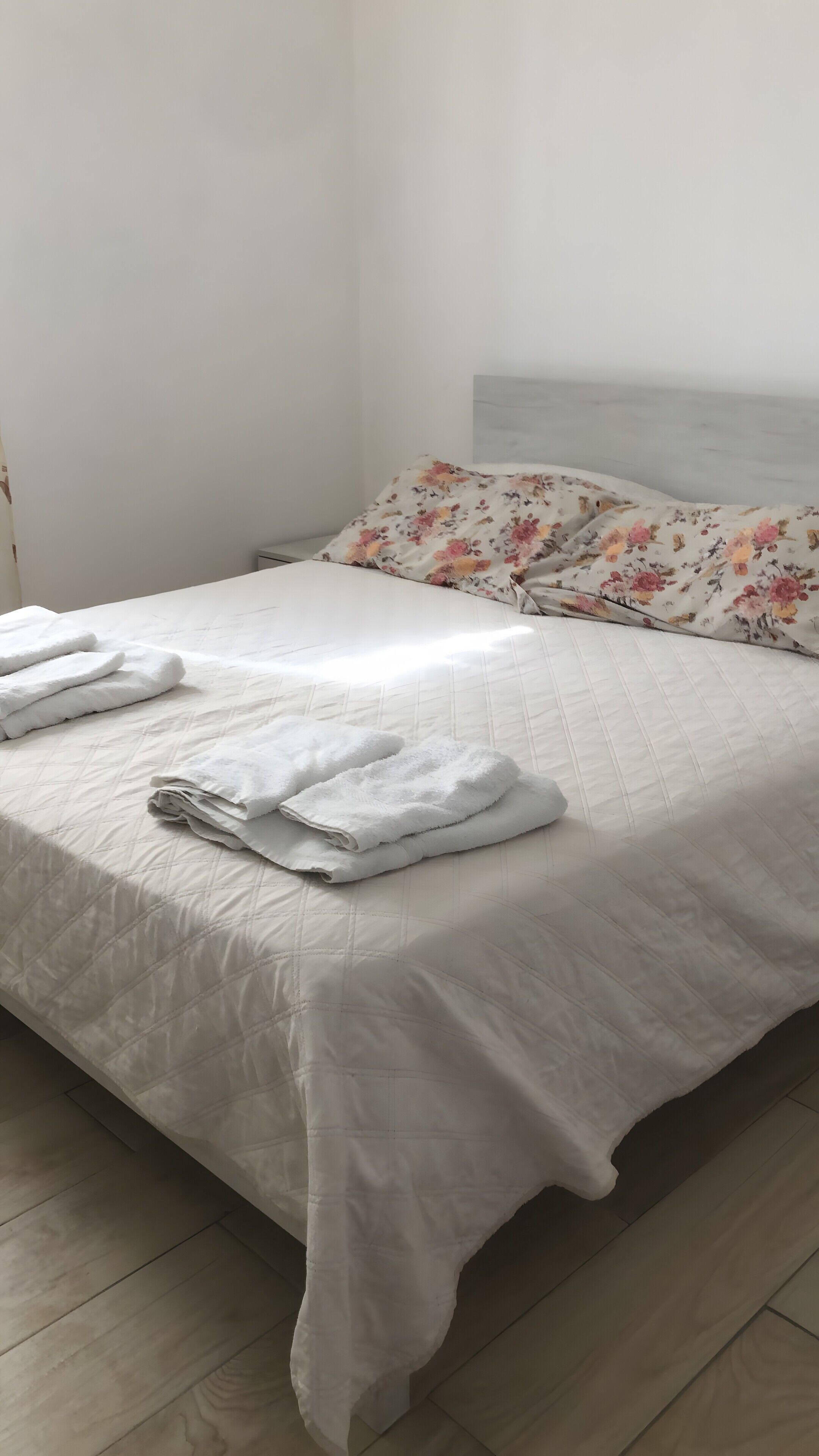 Ein ordentlich gemachtes Bett mit einem floralen Kopfkissen, einer weißen Decke und gefalteten Handtüchern.