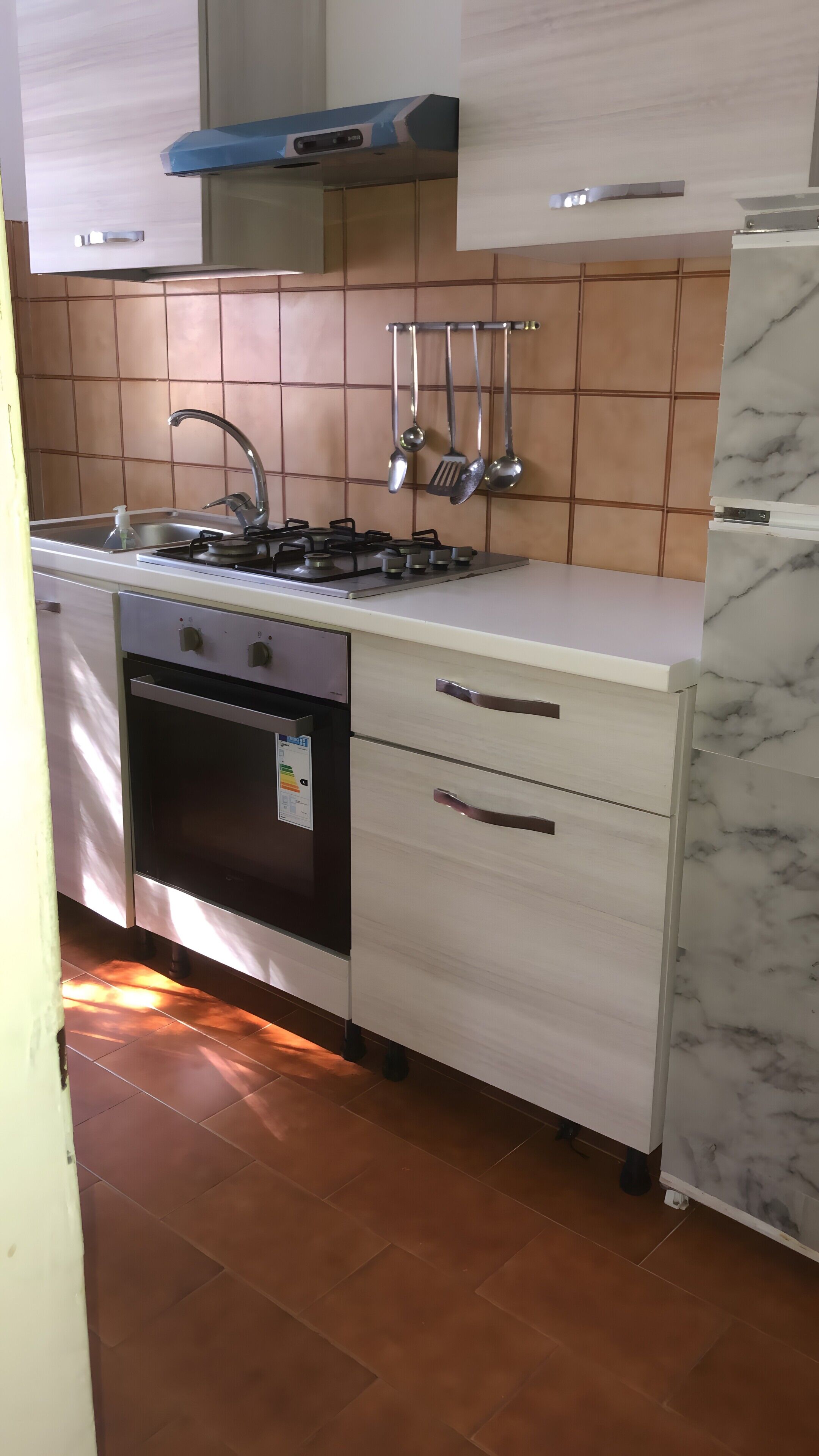 Eine Küche mit Gasherd, Backofen, Spüle und hängendem Kochgeschirr.