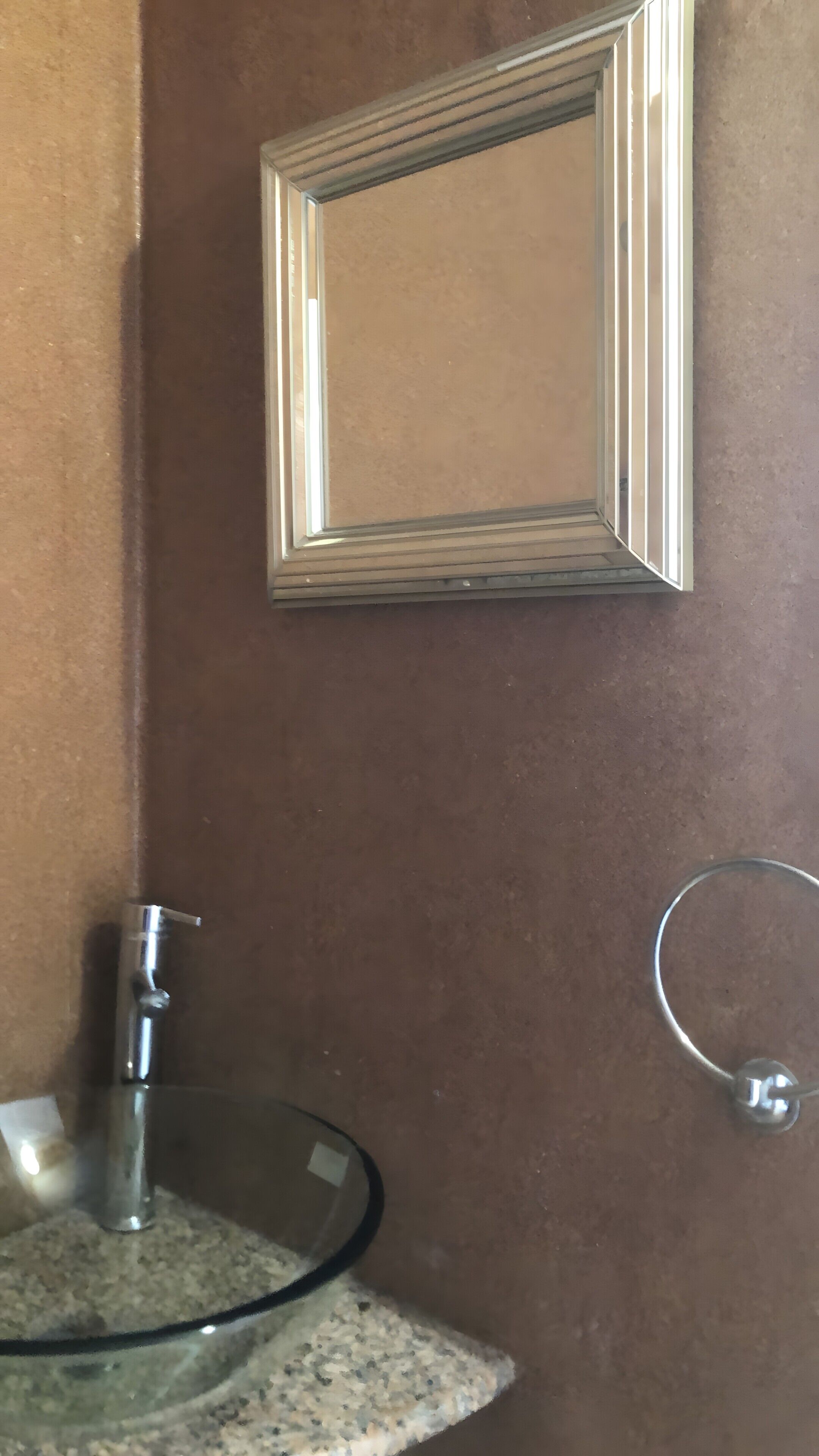 Un baño con lavamanos de vidrio, un espejo y un perchero para toallas.