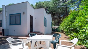 A small, white building with blue-framed windows and a door, surrounded by greenery and outdoor seating. - Property In A Holiday Village 'Monolocale 3 Posti Letto' with Shared Pool and Air Conditioning (peschici)