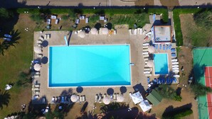 An aerial view of a resort with a large rectangular pool, sun loungers, umbrellas, and a tennis court. - Property In A Holiday Village 'Monolocale 3 Posti Letto' with Shared Pool and Air Conditioning (peschici)