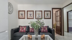 A living room with a black leather sofa, a white coffee table, a vase with flowers, and framed artwork on the wall. - Holiday Home 'Pepi Sánchez Conil' with Private Terrace and Wi-Fi (Conil de la Frontera)