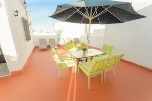An outdoor patio with a table and chairs, a large umbrella, and a white wall.