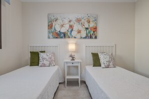 A bedroom with two beds, a nightstand, a lamp, and a floral painting on the wall.