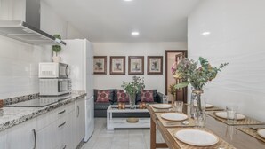 A modern kitchen with a microwave, toaster, and a dining area set for four with a table, chairs, and a vase of flowers. - Holiday Home 'Pepi Sánchez Conil' with Private Terrace and Wi-Fi (Conil de la Frontera)