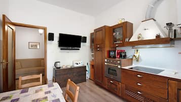 A compact kitchen with a flat-screen TV, wooden cabinets, a microwave, and a built-in oven.