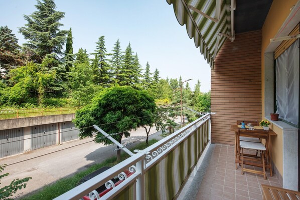 A balcony with a view of a road and trees, a wooden table with chairs, and a potted plant.
