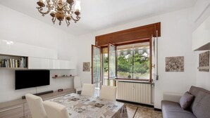 Una sala de estar moderna con mesa de comedor, sofá, televisor y ventanas amplias.