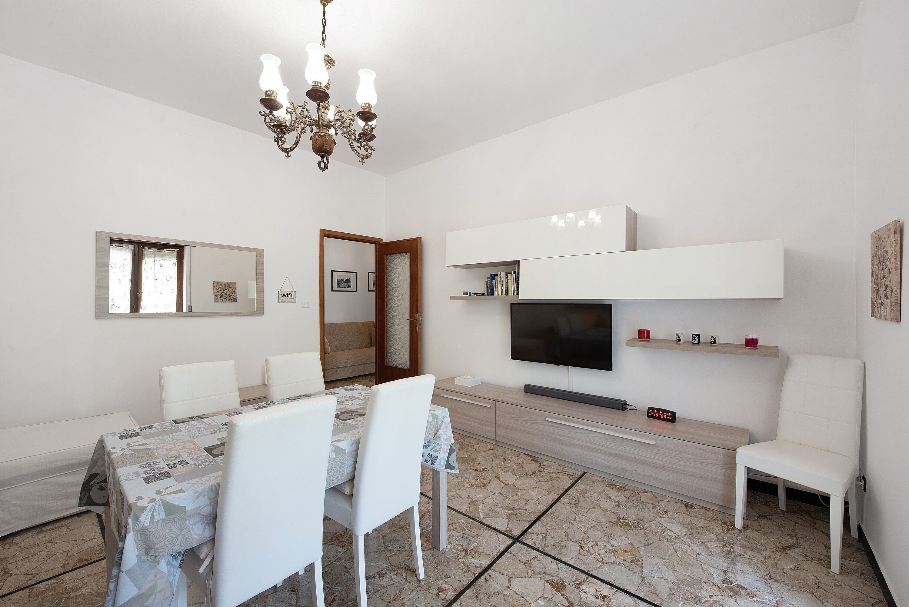 A dining area with a table, chairs, a chandelier, a TV, and a wooden cabinet.