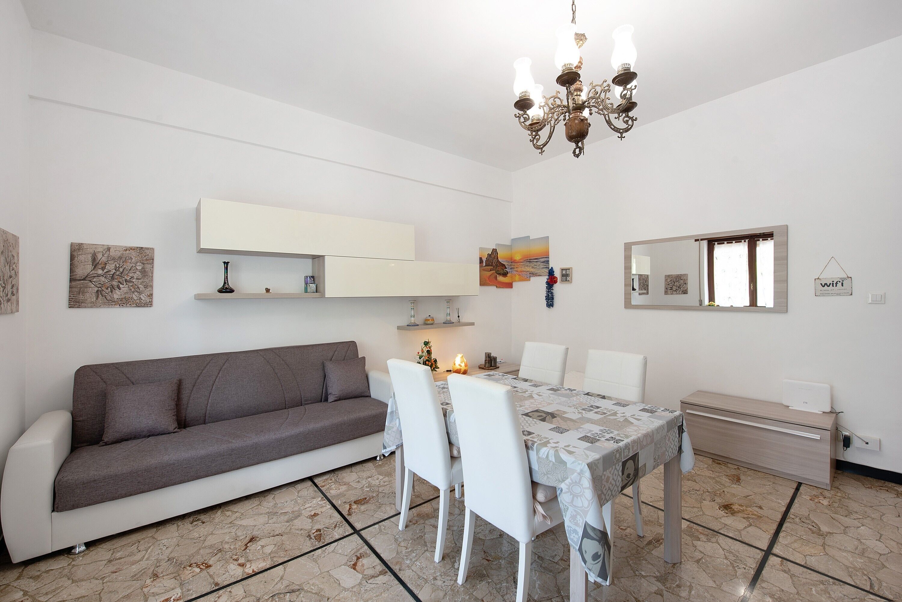 Ein modernes Wohnzimmer mit Sofa, Esstisch, Stühlen, einer Chandelieber, einem Kamin und Kunstwerken an den Wänden.