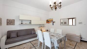 Ein modernes Wohnzimmer mit Sofa, Esstisch, Stühlen, einer Chandelieber, einem Kamin und Kunstwerken an den Wänden.