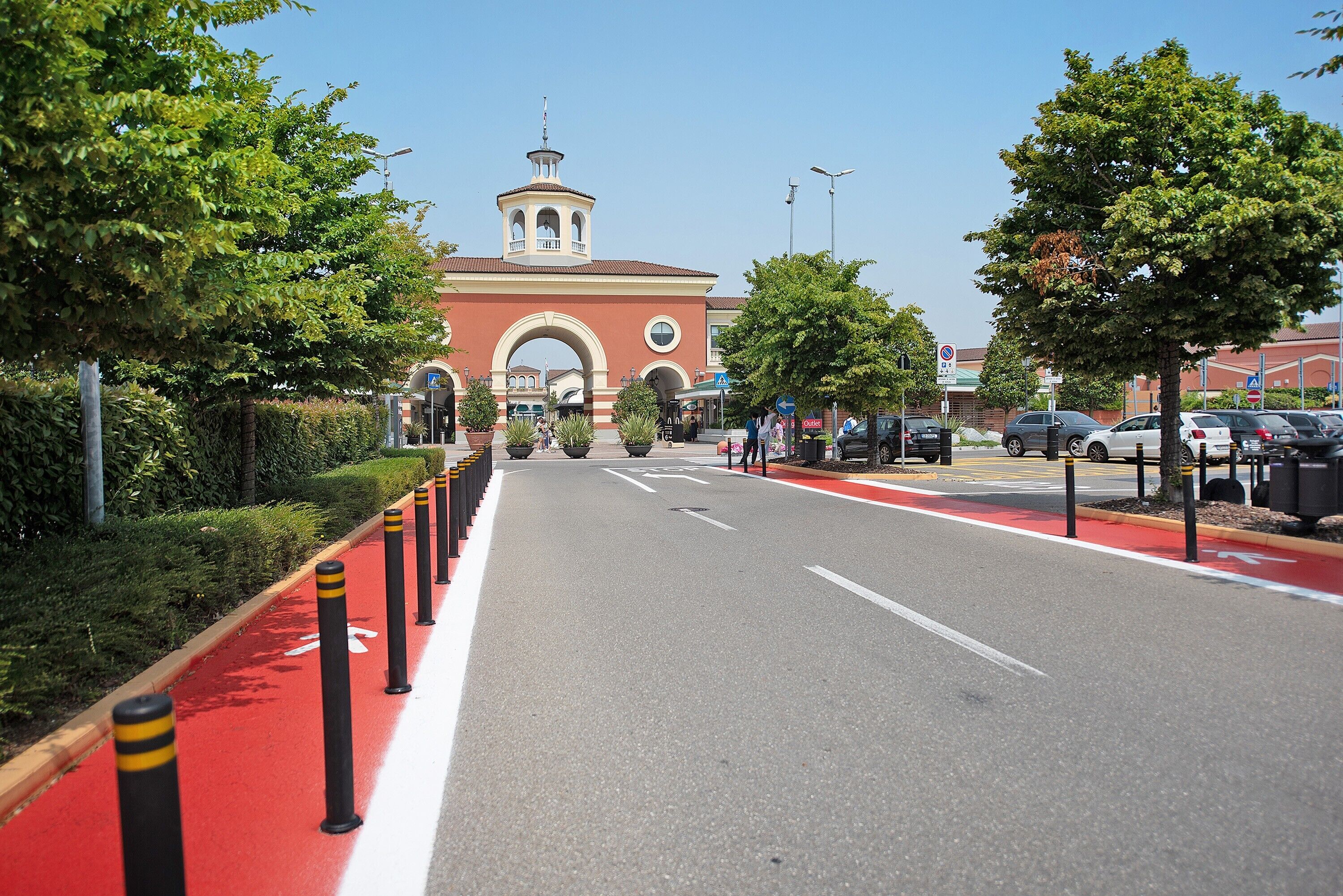 Una calle con carril bici rojo, bolardos y un edificio con una torre.