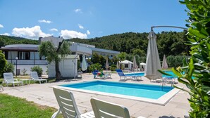 Ein Schwimmbad mit Liegestühlen, einer überdachten Liegefläche und einem Gebäude mit gewölbter Dachform.