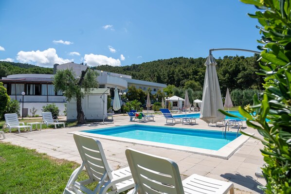 A swimming pool with lounge chairs, a covered area, and a building with a curved roof.