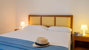 Ein ordentlich bezogenes Bett mit einer blauen Tagesdecke, ein Hut auf dem Bett und zwei Nachttischlampen auf Holznachtkästen.