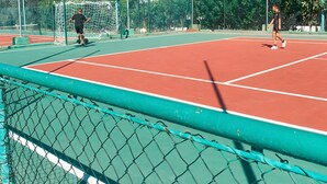 Ein Tennisplatz mit Netz, Tor und Bäumen im Hintergrund.