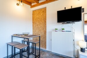 Une pièce comprenant une table et des chaises, un téléviseur fixé au mur, un radiateur et une fenêtre.