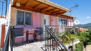 A pink building with a wooden balcony, a satellite dish, and a table with chairs. - Apartment 'Viola' with Mountain View, Wi-Fi and Air Conditioning (Agios Mattheos)