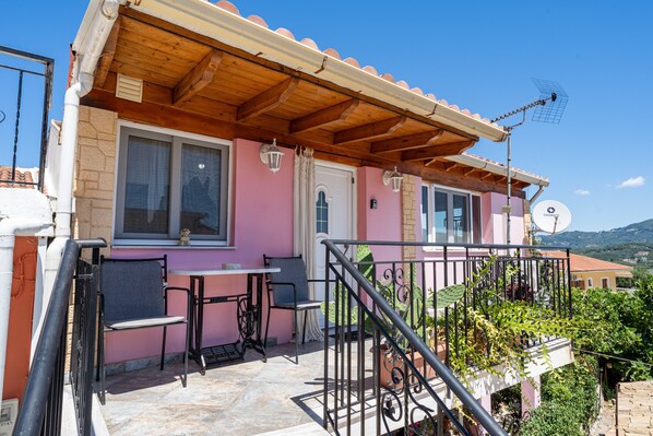 Un bâtiment rose doté d’un balcon en bois, d’une antenne parabolique et d’une table avec des chaises.