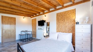 A bedroom with a bed, wooden ceiling beams, a TV, a dresser, and a small table with chairs. - Apartment 'Viola' with Mountain View, Wi-Fi and Air Conditioning (Agios Mattheos)