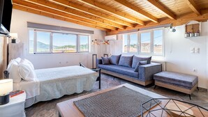 A room with a wooden ceiling, a sofa, a bed, and a view of the landscape. - Apartment 'Viola' with Mountain View, Wi-Fi and Air Conditioning (Agios Mattheos)