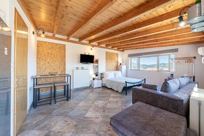 Une pièce avec un plafond en bois, un lit, un canapé, une table à manger avec des bancs, un téléviseur et une fenêtre donnant sur un beau paysage.