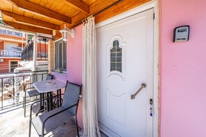Un balcon avec une table et des chaises, une porte blanche avec une fenêtre et un appareil fixé au mur.