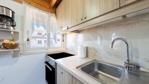 A kitchen with wooden cabinets, a stainless steel sink, a window with a view of buildings, and a dish rack. - Apartment 'Viola' with Mountain View, Wi-Fi and Air Conditioning (Agios Mattheos)