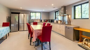 Una cocina moderna con electrodomésticos de acero inoxidable, una zona de comedor con sillas rojas y mantel a cuadros, y ventanas amplias que dejan entrar luz natural.