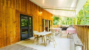 Un patio techado con paredes de madera, una mesa con sillas y una parrilla.