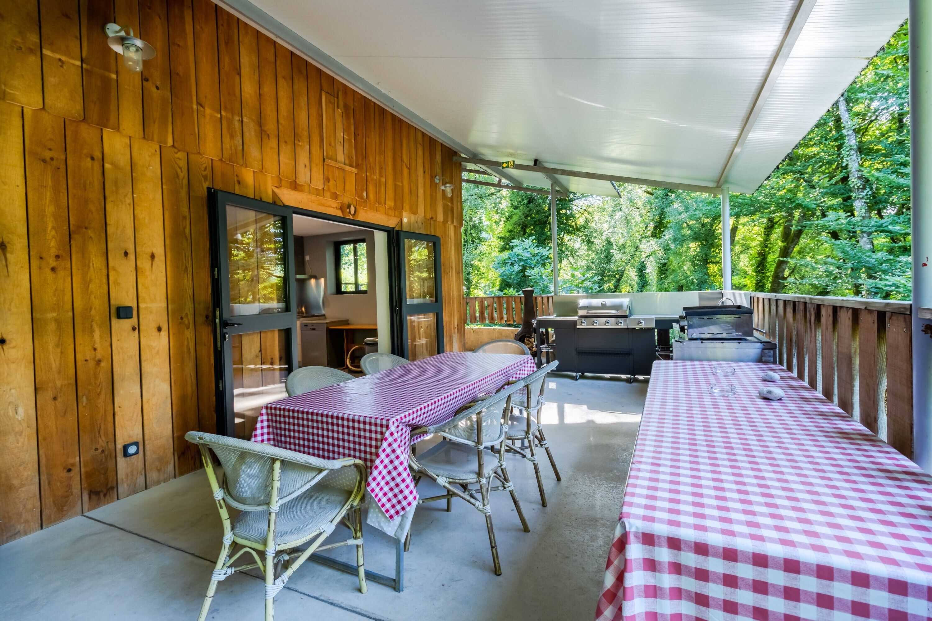 An outdoor patio with a covered seating area, a grill, and a table with a checkered tablecloth.