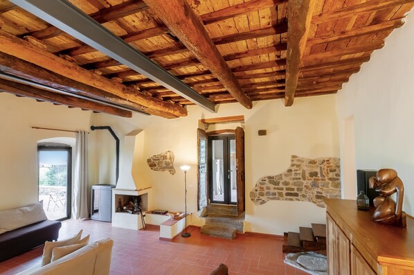 A rustic interior with a stone fireplace, wooden beams, a sofa, and a staircase leading to a door.