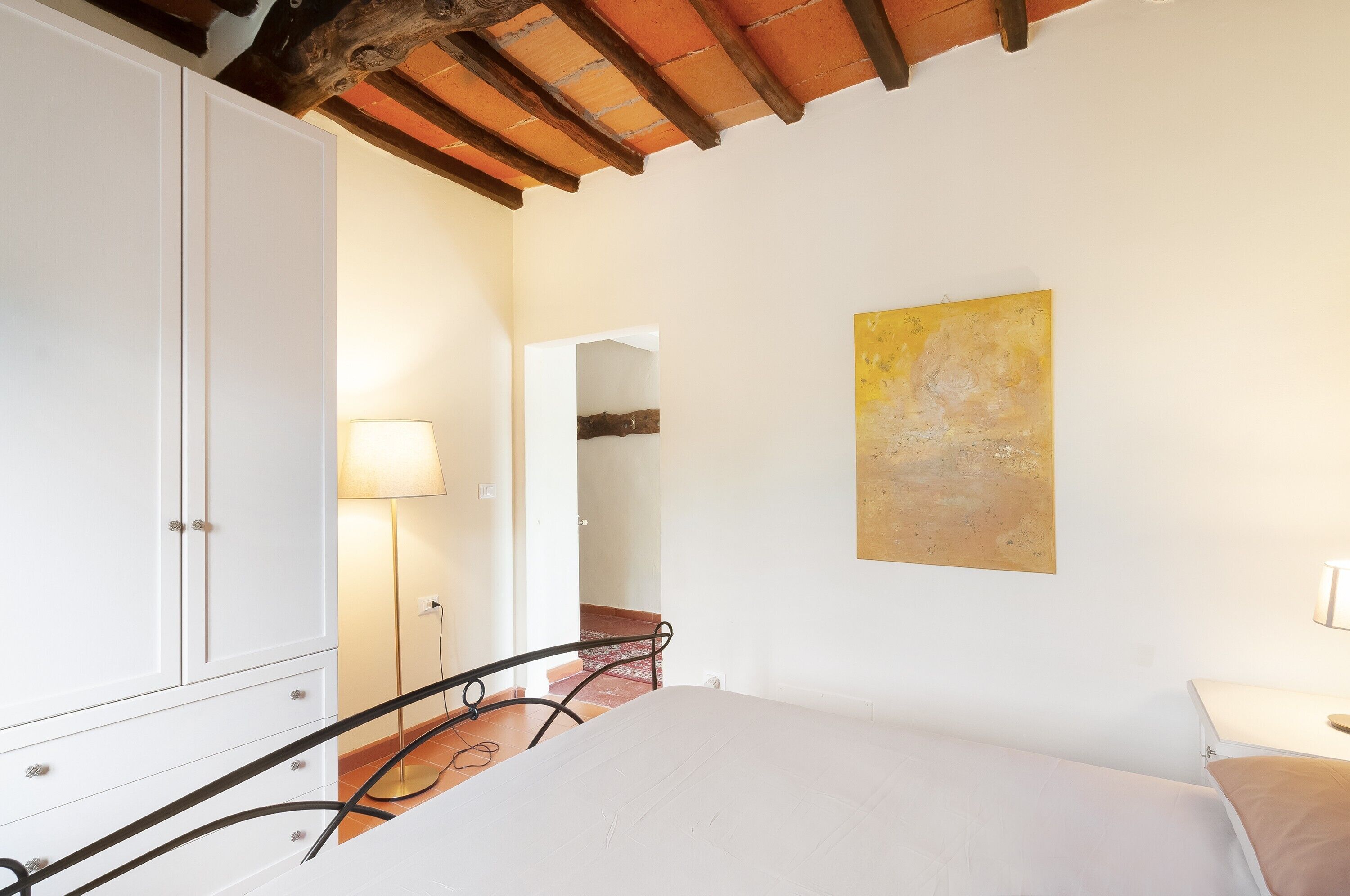 Une chambre à coucher avec un lit, une armoire, une lampe et un tableau au mur.