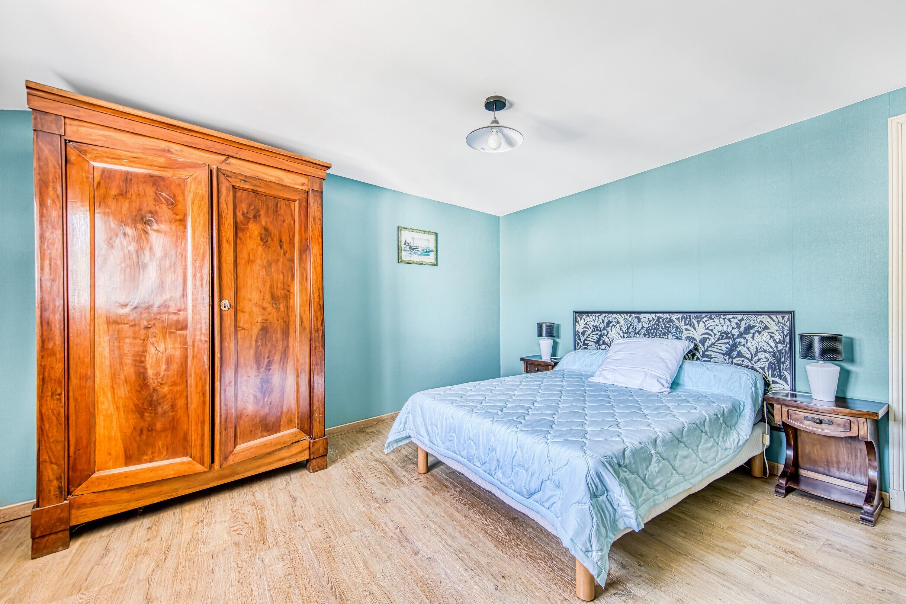 A bedroom with a bed, wooden wardrobe, and a nightstand.