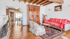 Uma sala de estar ampla com piso de madeira, um sofá vermelho, uma poltrona estampada e um grande armário de madeira.