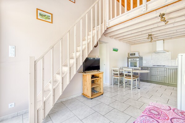 Una escalera conduce a una zona superior tipo loft, una cocina con electrodomésticos modernos y un comedor con mesa y sillas.