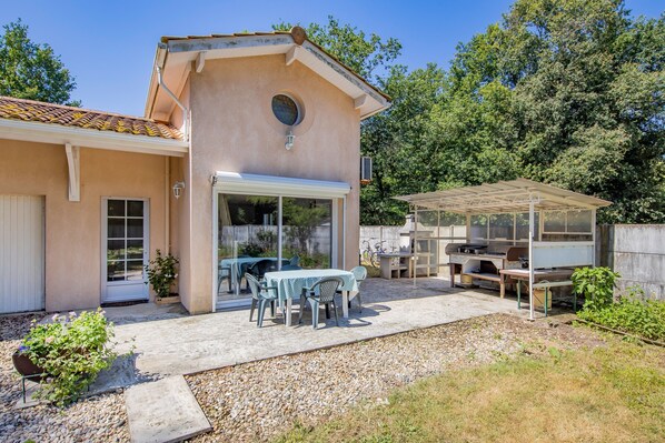 Una casa con patio, cocina exterior techada y una mesa con sillas.