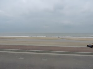 Een strand met een weg op de voorgrond en enkele mensen die langs de kust wandelen.
