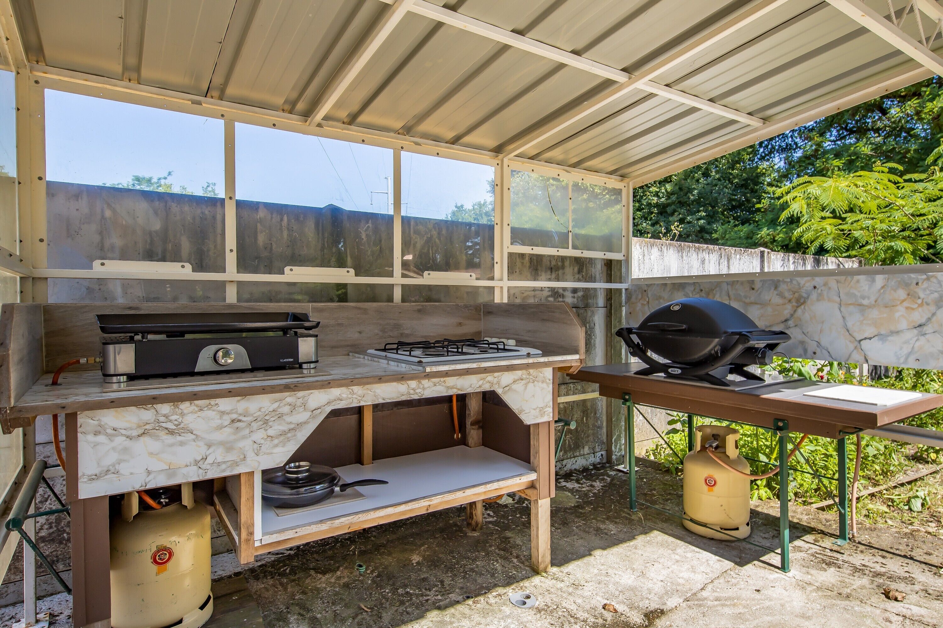 An outdoor kitchen with a gas stove, grill, and propane tank.