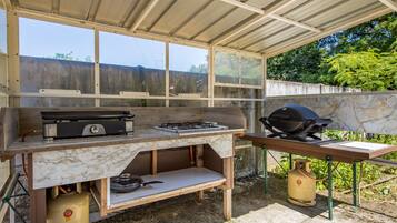 An outdoor kitchen with a gas stove, grill, and propane tank.