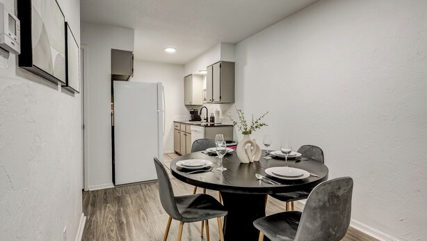 A modern dining area with a round table set for four, black chairs, and a vase with a plant. - Near Boone Pickens Stadium - Stillwater Stay (Stillwater)