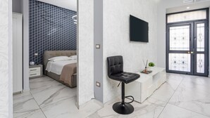 Camera d'albergo moderna con un letto, una scrivania, una sedia, una TV e una porta con un pannello in vetro.